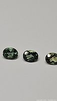 Three untreated mint green oval cut apatite gemstones displayed against a plain background, showing shape, color, and clarity
