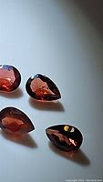 Four pear shaped cherry red Mozambique garnet gemstones shown on white background, highlighting their faceting and color.