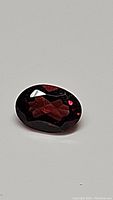 Close-up photo of the oval cut cherry red Mozambique garnet gemstone showing facets and color.