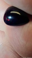 Close-up photo showing the jet black pear cabochon black opal with some visible reflection of light on its smooth surface.