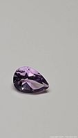 Purple pear cut amethyst gemstone on neutral background highlighting clarity and color.