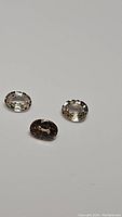 Three natural oval cut light champagne colored zircon gemstones on gray background, showing facets and clarity.