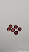 Six round cabochon garnet gemstones arranged on a white background, showing smooth polished surfaces and pink-orange coloration.