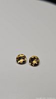 Pair of round cut natural golden citrine gemstones on plain background showing faceting and color.