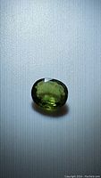 Oval green sapphire gemstone with dark green color on light background, showing facets and good luster.