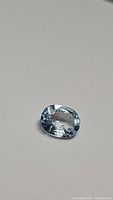 Oval cut natural lagoon blue aquamarine gemstone photographed against a neutral background showing its clarity and color.