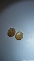 Photo showing two round peach moonstone cabochons with cat's eye effect on a gray surface.