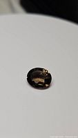 Close-up photo showing oval cut natural smokey quartz gemstone on white background with visible facets and reflections.