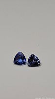 Pair of natural trillion cut Tanzanite gemstones showing strong blue-purple color and clarity, on neutral background.