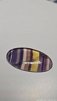 Close-up photo of a polished oval-shaped rainbow fluorite gemstone showing color bands and surface reflections.