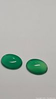 Two vivid lime green onyx oval cabochon stones with smooth surfaces shown on white background.