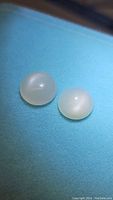 Two round natural white moonstone cabochons placed on a blue background, showing smooth domed cabochon cut and soft white translucency with internal flash effect.