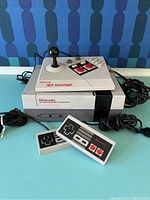 Full view of the Nintendo Entertainment System console with NES Advantage joystick and two wired controllers placed in front.