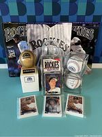 Full view of lot showing wooden baseball trophy, team scorecard magazines, sealed and loose Rockies baseball cards, and three baseballs in protective cubes.