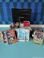 Photo of a black storage box filled with football trading cards including loose cards and mini card albums from various teams like Green Bay Packers and Dallas Cowboys.