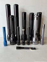 All 13 Mag-Lite flashlights arranged standing on flat surface, showing variety in size and color