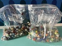 Two ziplock bags filled with various vintage marbles showing a range of colors and types on a teal surface with a blue polka dot background.