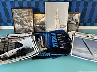 Wide view of lot showing framed photos, magazines, colorful t-shirts, and loose photography prints of Titan missiles on display on a blue surface.