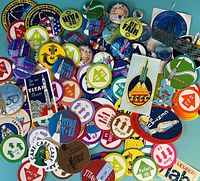 Overview photo showing large assortment of various circular pins and stickers, some with rocket launch images, colorful text, and slogans related to Titan missile program.