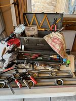 Photo showing assembled lot arranged on table with Craftsman toolbox open, multiple levels, clamps, hand drill, hand tools, doweling jig kit, shop light.