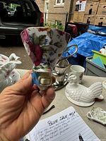 Hand holding a ceramic half teacup night light with colorful floral pattern, attached to a plug base with a light bulb cover.