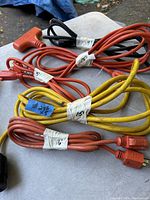 Photo showing five extension cords coiled and tagged with length labels. Two orange 15-foot cords, one orange 9-foot cord, one orange 5-foot cord, and one yellow 6-foot cord are visible.