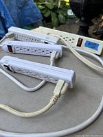 Four power bars laid out on a gray surface outdoors, showing the power bars with multiple outlets and red switches.