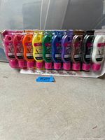 Photo showing 10 tubes of Tulip Soft fabric paint in various colors arranged side by side in original packaging on a beige surface.