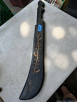 Top view of the wooden sheath showing black color with painted decorative gold-colored designs and a slight curve. The sheath measures about 28 inches long.