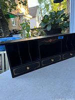Full view of black lacquered antique pigeon hole desk organizer with three pigeon hole compartments on the left, a central open space, and three drawers with brass knobs below, decorated with floral patterns.