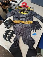 Full view of costume including padded jumpsuit, gloves, mask, and batarangs laid out on table
