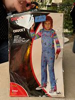 Packaged Halloween Chucky child costume in bag with attached shirt showing front model image and branding.