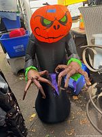 Full view of the Halloween inflatable showing the orange pumpkin head with angry green eyes and black-caped body with green cuffs and purple waist accents, and long clawed hands.