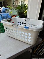 White Sterilite laundry basket with handles and ventilation holes sitting on a table outdoors.