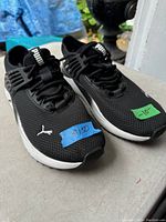 Front pair view of black Puma running shoes with white soles, size 10 markings on tape attached to shoes.