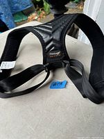 Black adjustable posture corrector with padded shoulder straps and back support, labeled 'Thought'.