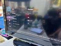 Photo of the Samsung TV powered on showing picture settings menu including Mode, Backlight, Contrast, Brightness, Sharpness, and Aspect Adjustment to confirm screen size and working condition.