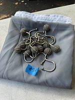 Photo shows folded gray fabric shower curtain with white liner underneath, topped with 12 metal shower curtain hooks. Hooks are S-shaped with gray round decorative ends.