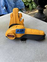 Side view of the yellow and black Smith's electric sharpener showing the brand label and the plug, placed on a gray surface outdoors.