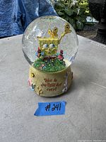 Clear glass snow globe featuring SpongeBob SquarePants holding a butterfly net and butterfly inside. Base decorated with sea-themed elements and text reading 'This is the Best Day Ever!'. Glitter inside the globe.