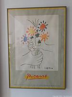 Full view of the framed Picasso poster showing colorful flower bouquet held by hands, set in gray-green metal frame with glass.