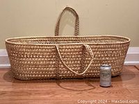 Front view of large natural wicker basket with two handles and a can placed beside it for scale.