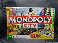 Front of Monopoly City box showing the game's metropolitan city theme, Mr. Monopoly mascot and 80 3-D buildings feature