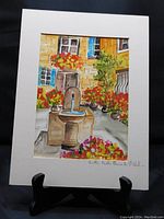 Frontal view of the original watercolour painting with white mat showing a stone drinking fountain, surrounding flowers, and architectural backdrop in vibrant colors.
