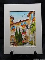 Full view of the watercolor painting with white matting, showing detailed colorful street scene with drinking fountain and flowers.