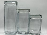 Set of three square clear glass canisters with snug fitting lids, varying in height, arranged side by side