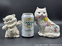 Two white ceramic cat items displayed with a Canada Dry soda can for size comparison, showing the smaller cat figurine and larger cat planter.