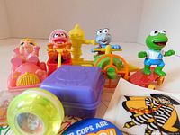 Muppet Babies toys in original packaging, three figures in small vehicles and one standing figure, plus purple case and round green spinning toy.