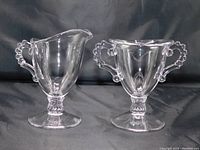 Clear glass creamer and open sugar bowl set with candlewick handles and pedestal bases displayed against a black background