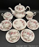 Full set showing teapot, sugar bowl, creamer, 4 teacups, 4 saucers, and 4 small plates with pink and purple floral pattern and gold trim.